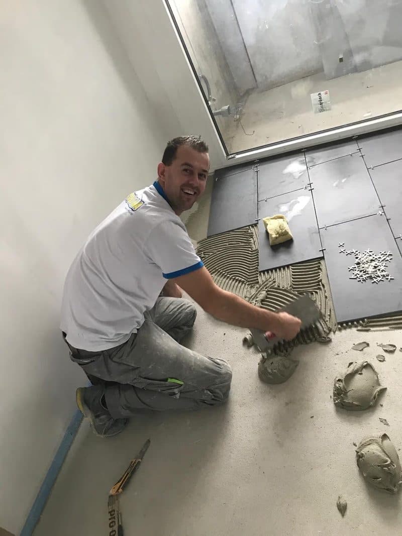 Suad Hasani, fondateur de Carrelage Concept, pose un carrelage de sol sur un chantier à Nyon